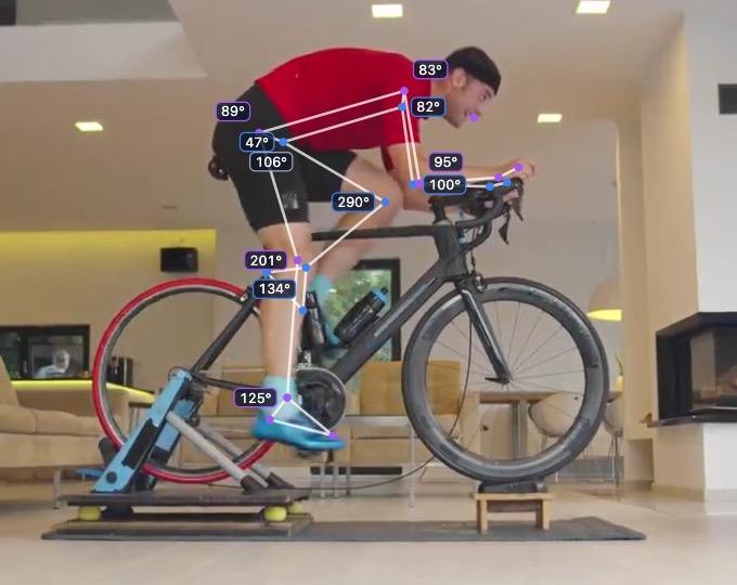 A rider on an indoor trainer, filmed side-on, with the tracked skeleton and joint angles drawn over the video.