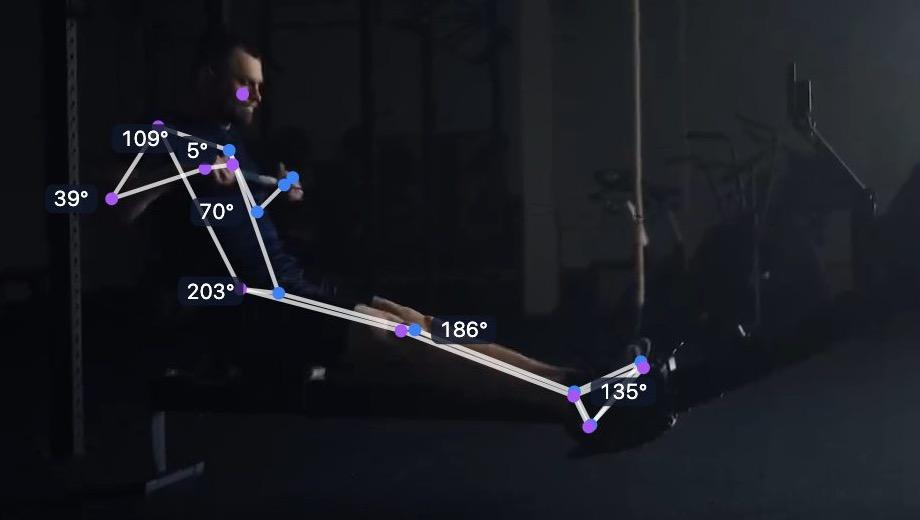 A rower at the finish of the stroke on an indoor rowing machine, with the tracked skeleton and joint angles drawn over the video.